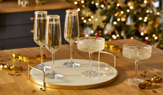 Plateau avec des flûtes à champagne remplies de boissons pétillantes, posé sur une table en bois et un sapin de Noël décoré en arrière-plan.