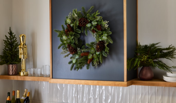 Étagère de cuisine ornée d'une couronne, d'un petit sapin de Noël, de verdure et d'un casse-noisettes, sur fond de dosseret sombre.