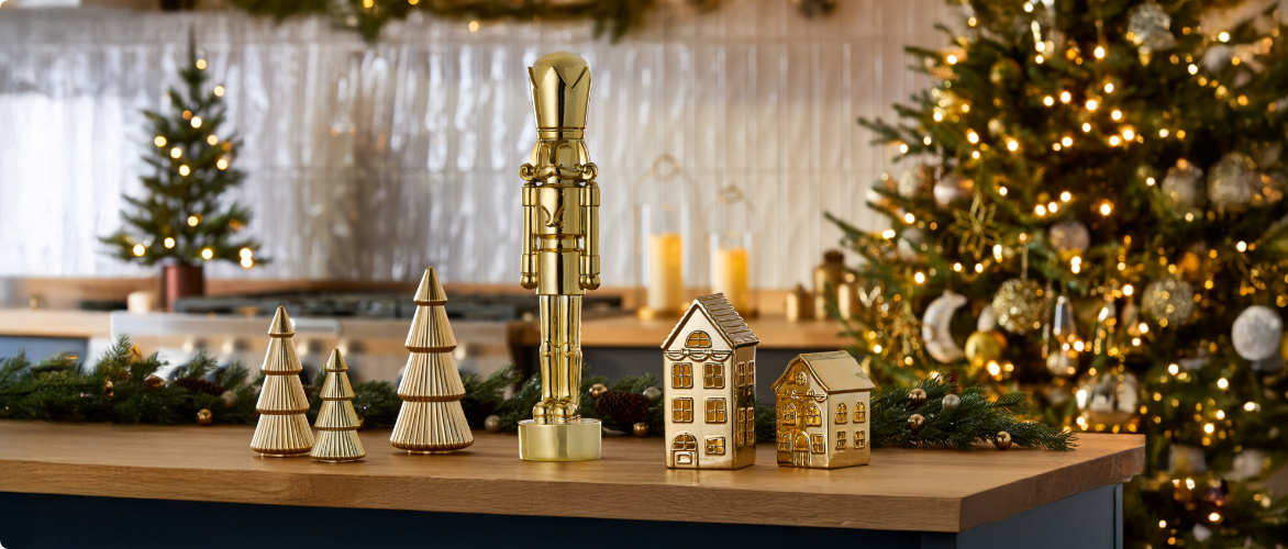 Décorations de Noël dorées sur un îlot de cuisine, dont des petits sapins, un casse-noisette et des maisonnettes.