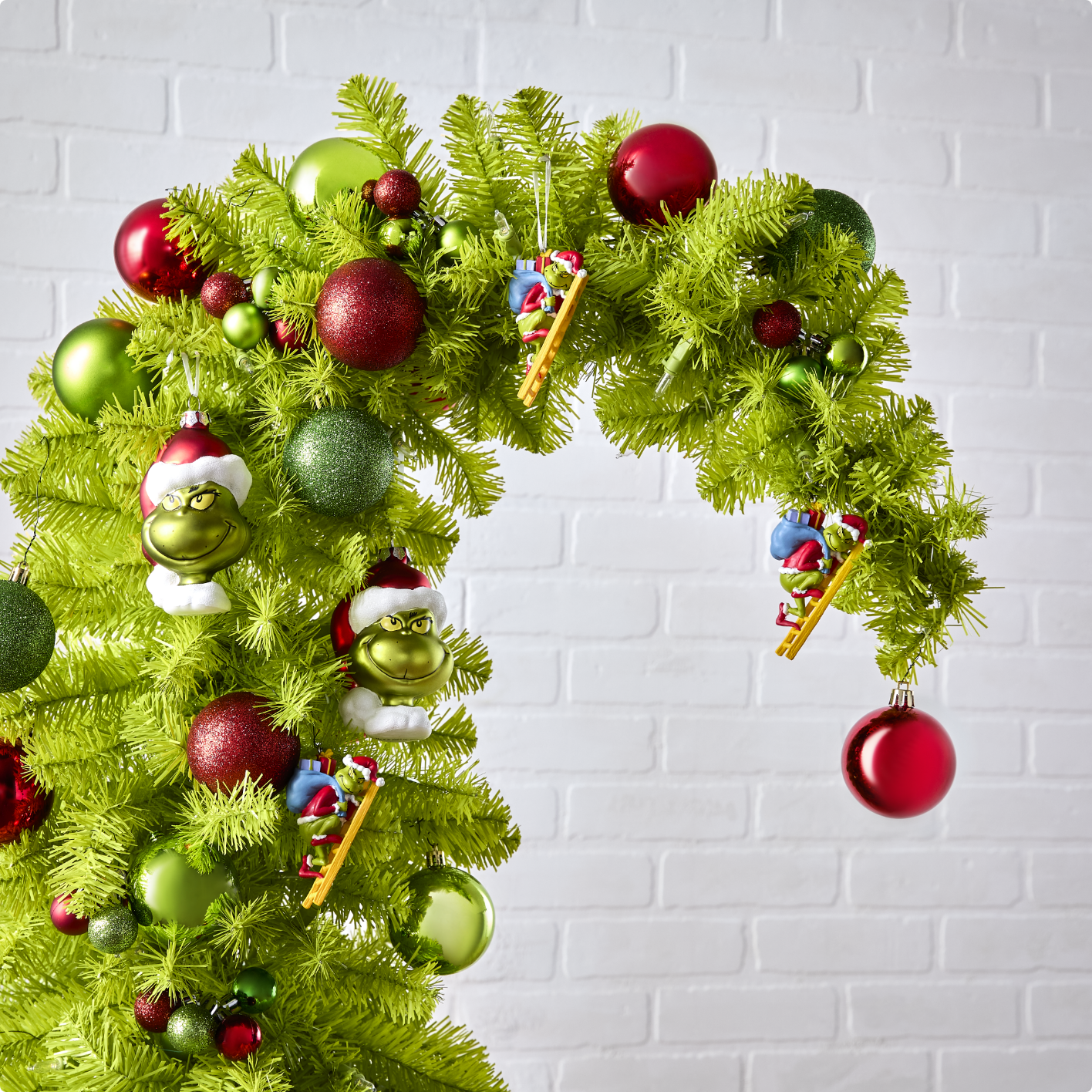 Un assortiment de mini ornements incassables Le Grincheux, de décorations en résine du Grincheux sur une échelle et de décorations Le Grincheux en verre soufflé sur un arbre Crumpit For Living inspiré du Grincheux.