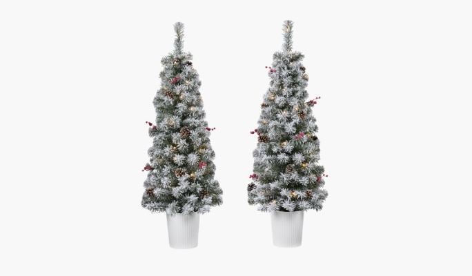 Deux sapins de Noël artificiels recouverts de neige dans des pots blancs, décorés de baies rouges et de lumières.