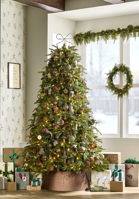 A decorated Christmas tree with presents underneath in a cozy room, featuring a wreath on the window and garland above it.