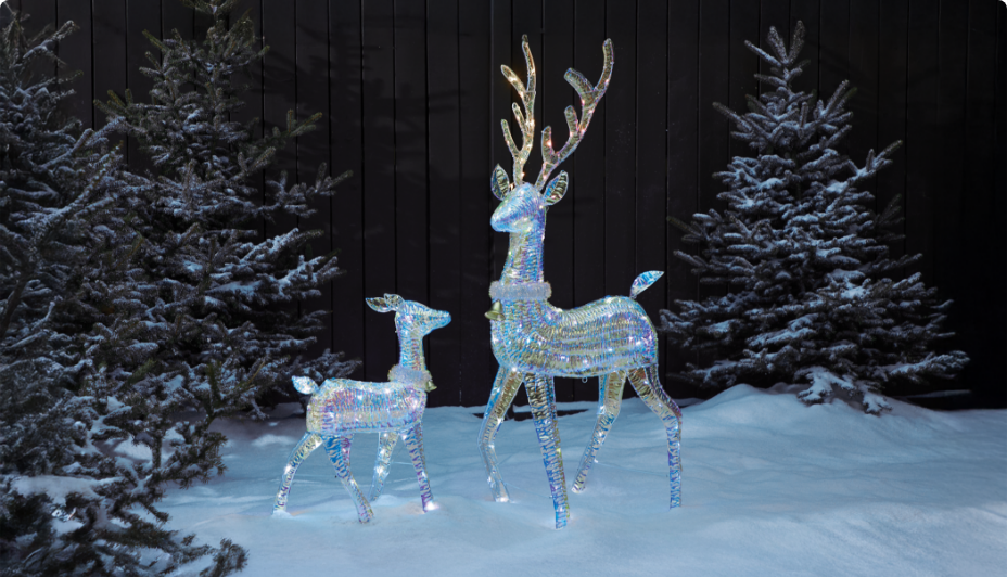 Two light-up reindeer decorations in a snowy outdoor setting, surrounded by snow-covered trees.