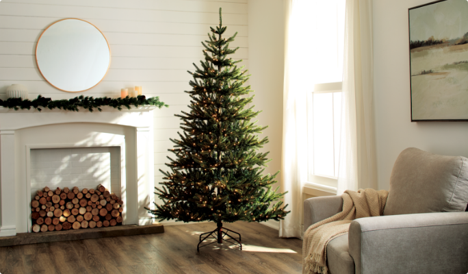Lit Christmas tree in a cozy living room with a fireplace, mirror, candles, and a comfy chair by the window.
