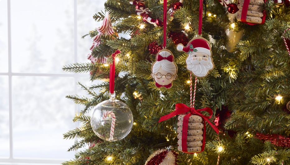Close-up of Christmas tree ornaments including a candy cane inside a glass ball, a stack of cookies tied with a bow, Santa, and Mrs. Claus.