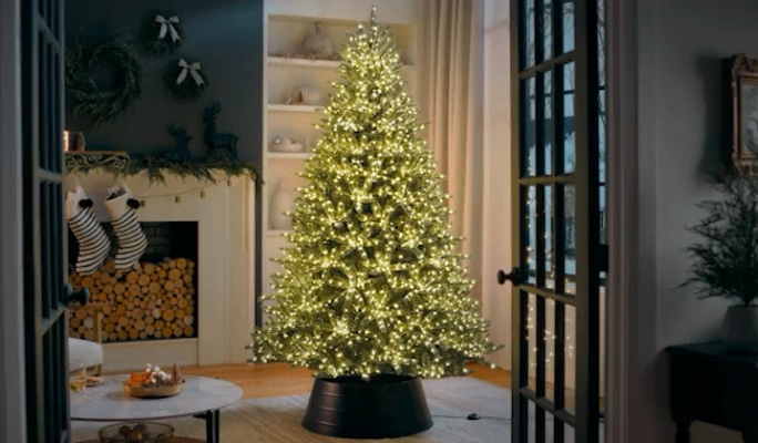 Lit Christmas tree in a cozy living room with a fireplace, stockings, and holiday decor.