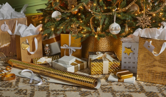 Gold and white gift wrap and decorations under a Christmas tree.