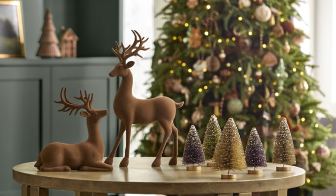 Indoor Christmas decor featuring reindeer figurines and a decorated Christmas tree on a wooden table.