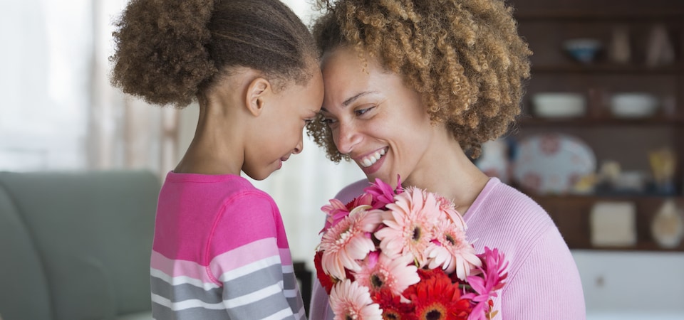 A child gives a bouquet of colorful flowers to an adult with curly hair. 