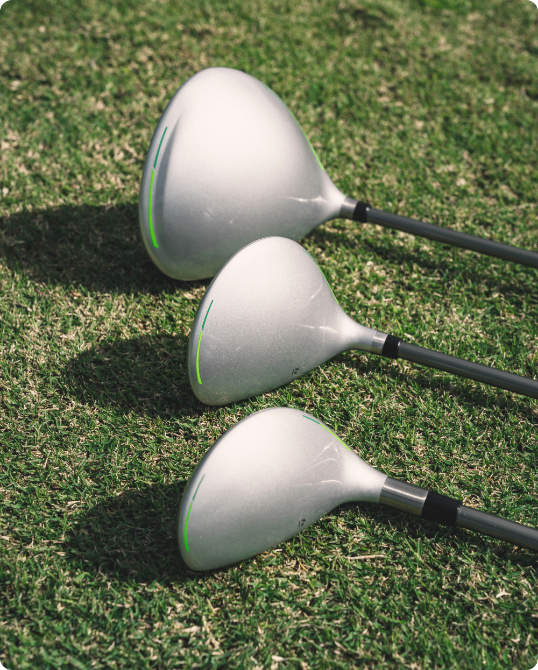  Three golf clubs laid on a grassy surface.
