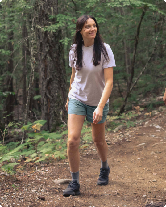 A person wearing a white t-shirt, shorts, and hiking boots walking on a forest trail.
