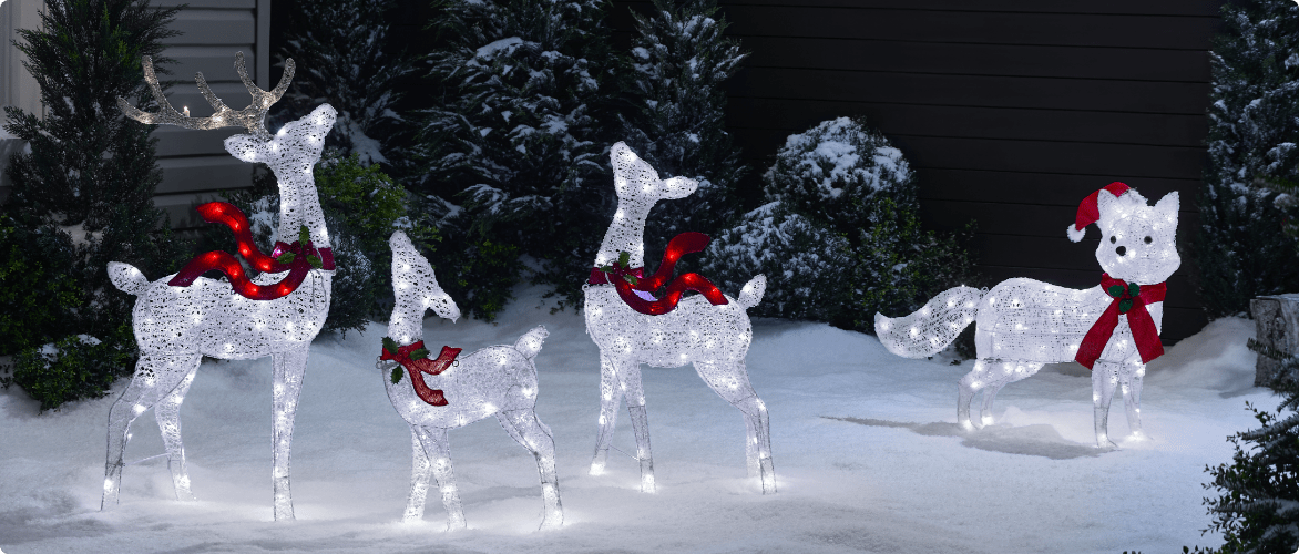 A snowy yard decorated with illuminated Christmas figures, including three reindeer and a fox wearing a Santa hat and scarf.
