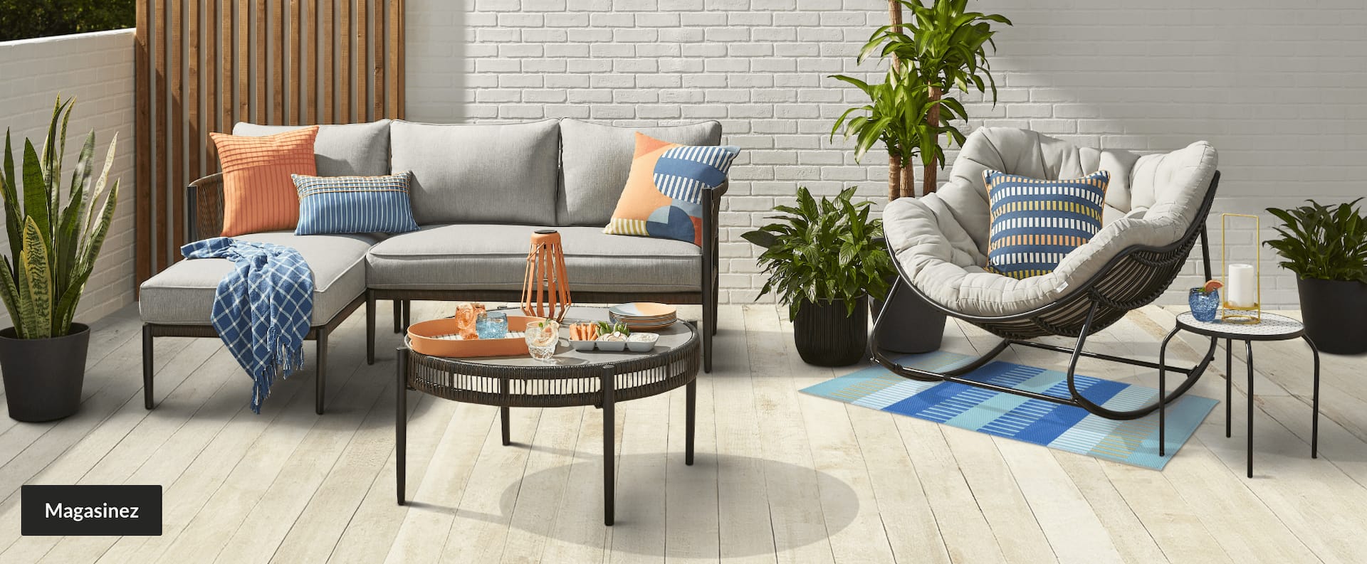 Un ensemble modulaire de jardin, une chaise, une table basse et une table d’appoint sur une terrasse, le tout habillé d’accessoires colorés.