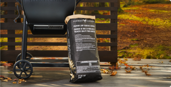 A bag of charcoal leaning on a BBQ on a deck.