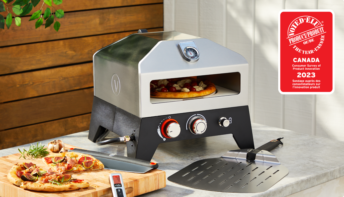 Un four à pizza au gaz Vida par PADERNO dans lequel cuit une pizza sur une table, avec une pizza cuite sur une planche à découper à côté.