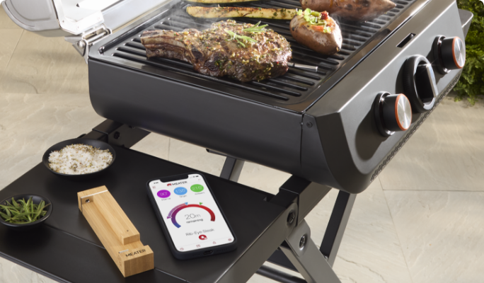 A MEATER® Pro Wireless Meat Thermometer on a BBQ side table next to a smart phone.