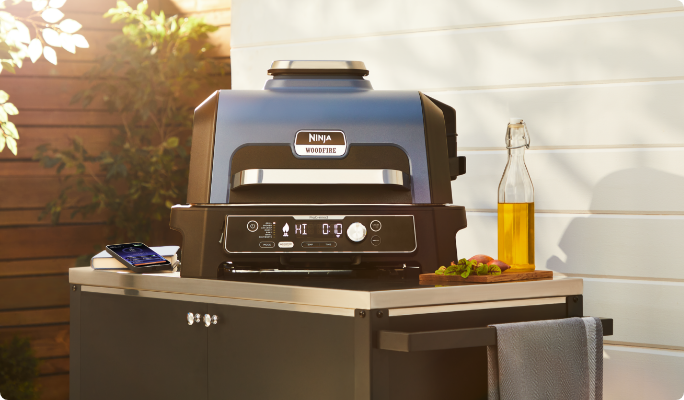 A Ninja Woodfire™ Pro Connect 7-in-1 Smart Outdoor Electric Grill on a table.