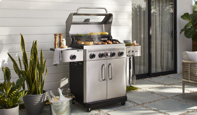 A Vida by PADERNO Essence Series 4-Burner Convertible BBQ on a back patio next to a sliding door and plants.