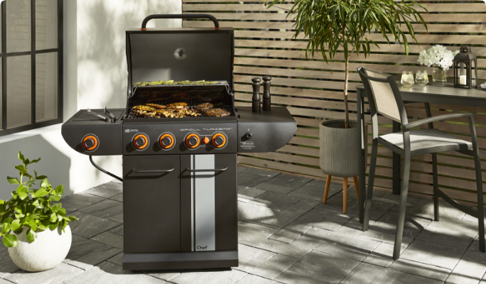 A MASTER Chef Grill Turismo 4-Burner Grill cooking foods on a patio next to a bar height patio table and chair.