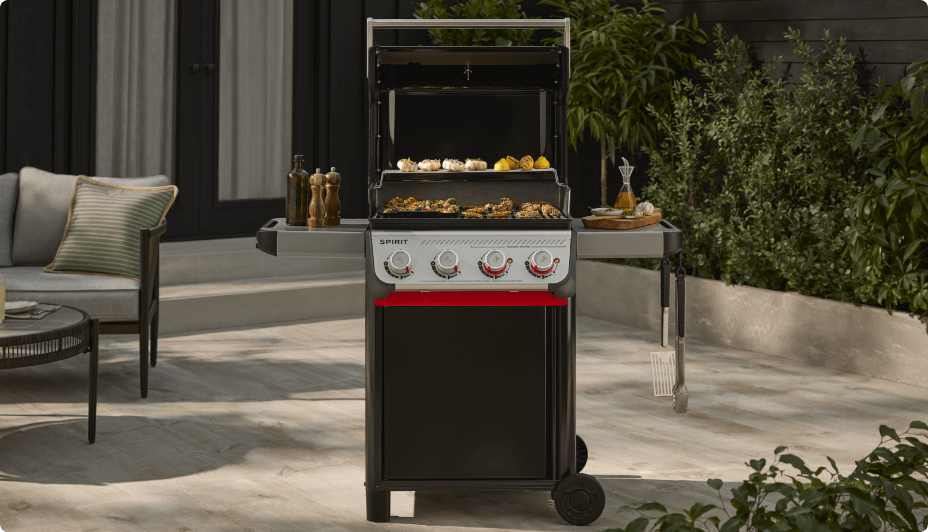 A Weber Spirit E-425 4-Burner Propane BBQ cooking foods on a patio.