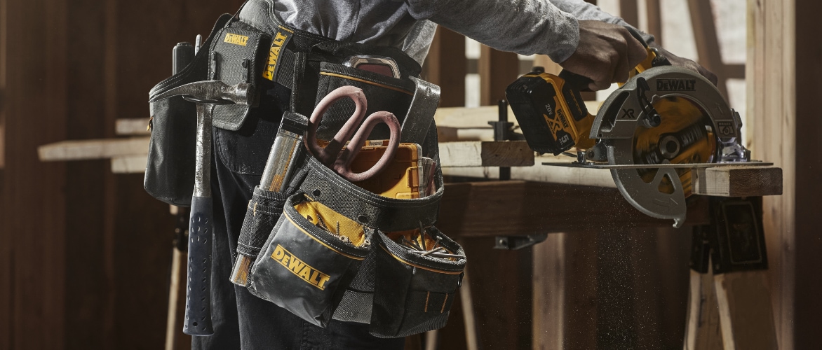 Un entrepreneur portant une ceinture porte-outils DEWALT coupe du bois à l'aide d'une scie circulaire.