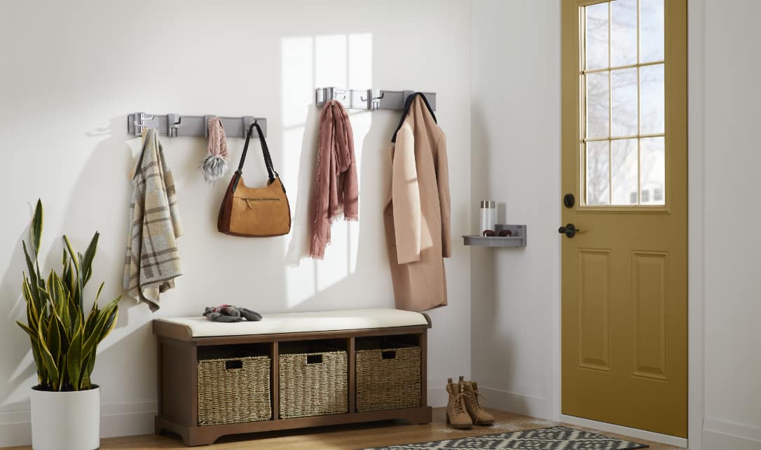 Entryway with coat hooks, a bench with storage baskets, and a yellow door.
