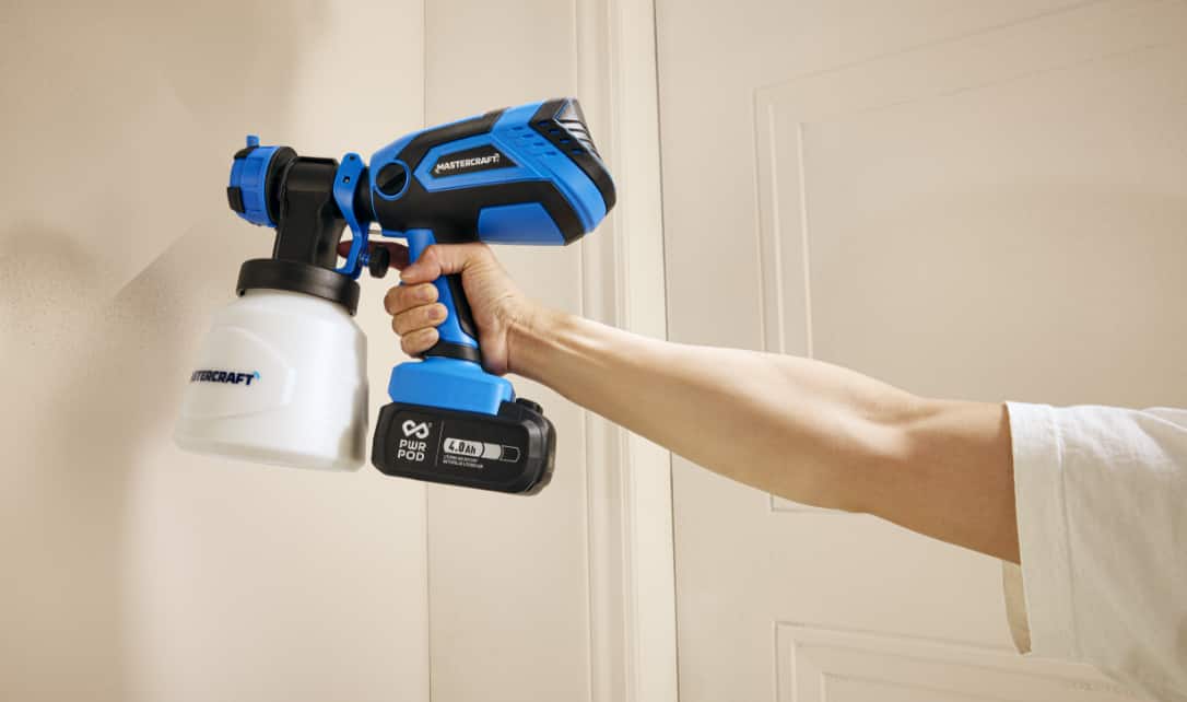 Person using a handheld paint sprayer on a wall.