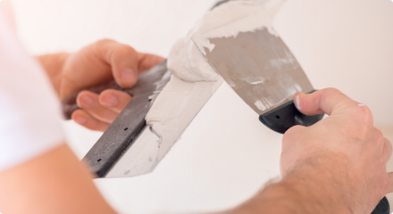 Close-up of a person applying joint compound to a putty knife.