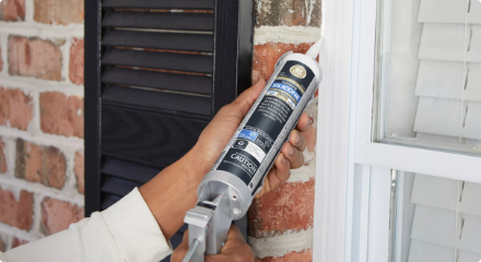 A person applying caulking to an exterior window frame.