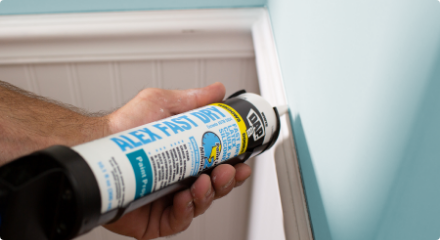 A person applying white caulking to wall trim.