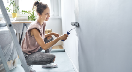 A person applying grey paint to a white wall with a roller.
