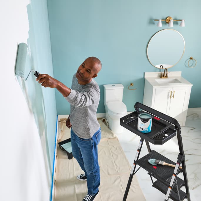 A woman using a roller to paint a light blue wall.