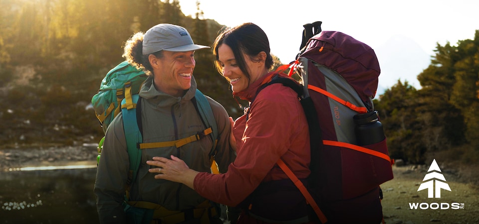 Two hikers with backpacks standing in a scenic outdoor location at sunset.