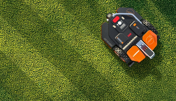 Une tondeuse robot Worx orange et noire tond la pelouse bien entretenue