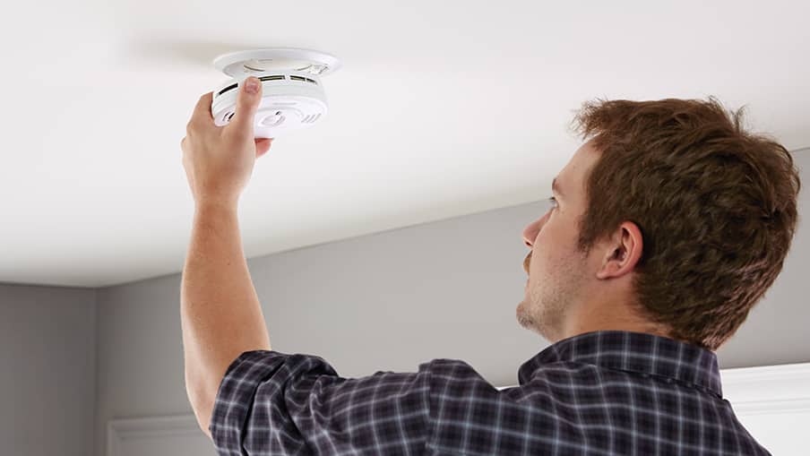 Person installing smoke alarm on ceiling