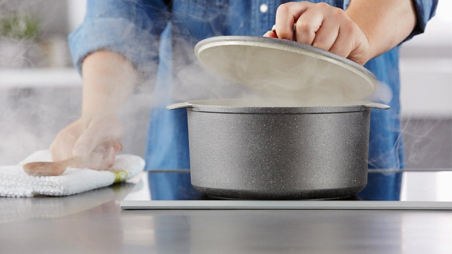 Une personne ouvrant une casserole sur la cuisinière et laissant échapper de la vapeur.