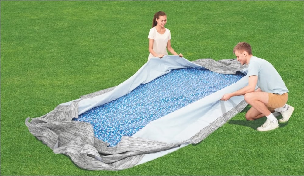 Two adults laying out the liner of a steel frame pool in a backyard. 
