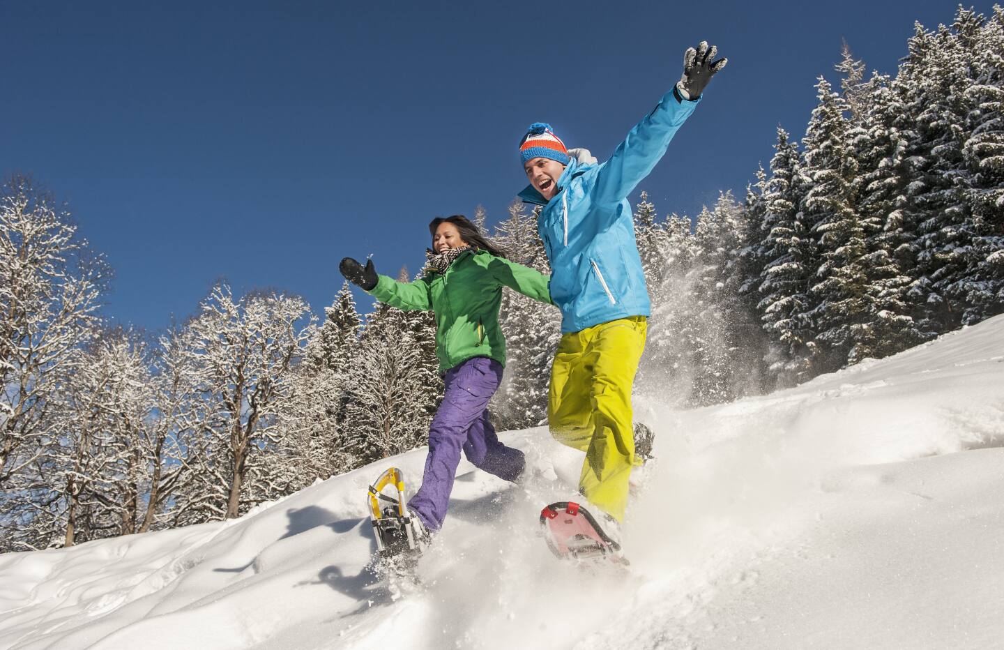 Two adults snowshoeing on a hill. 