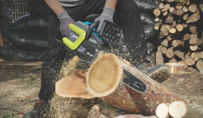 An adult cutting a log with a Yardworks 48V 16-in Chainsaw.