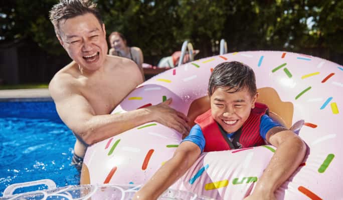 Un homme et un enfant dans un flotteur gonflable en forme de beigne Stella & Finn jouant dans une piscine.
