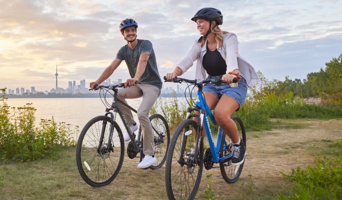 Two adults riding bicycles on a waterfront trail.
