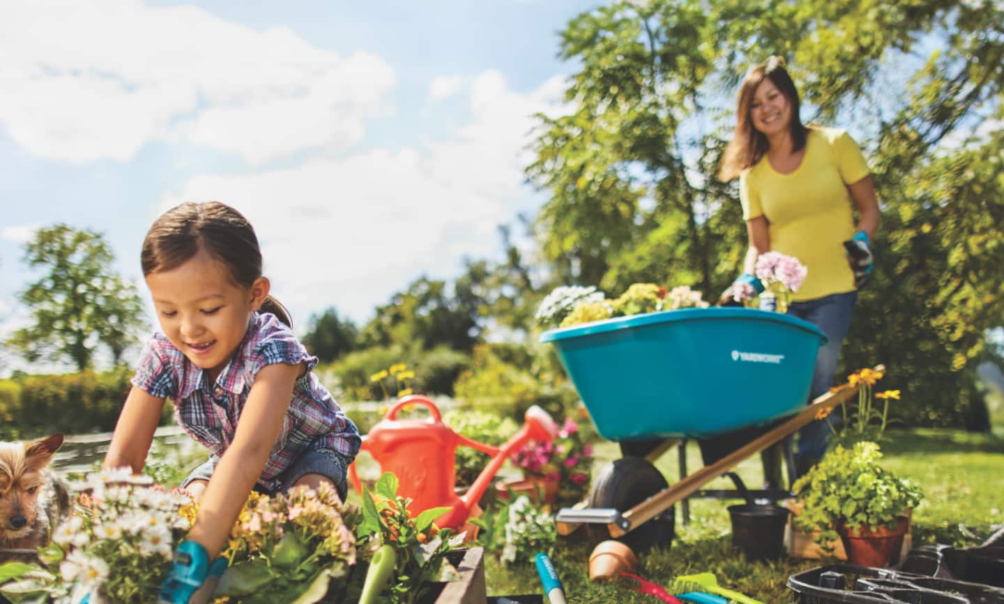 A woman and a child gardening with a Yardworks wheel barrow and other tools. 