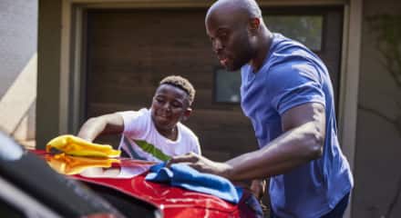 An adult man and a young boy wash a red car together.