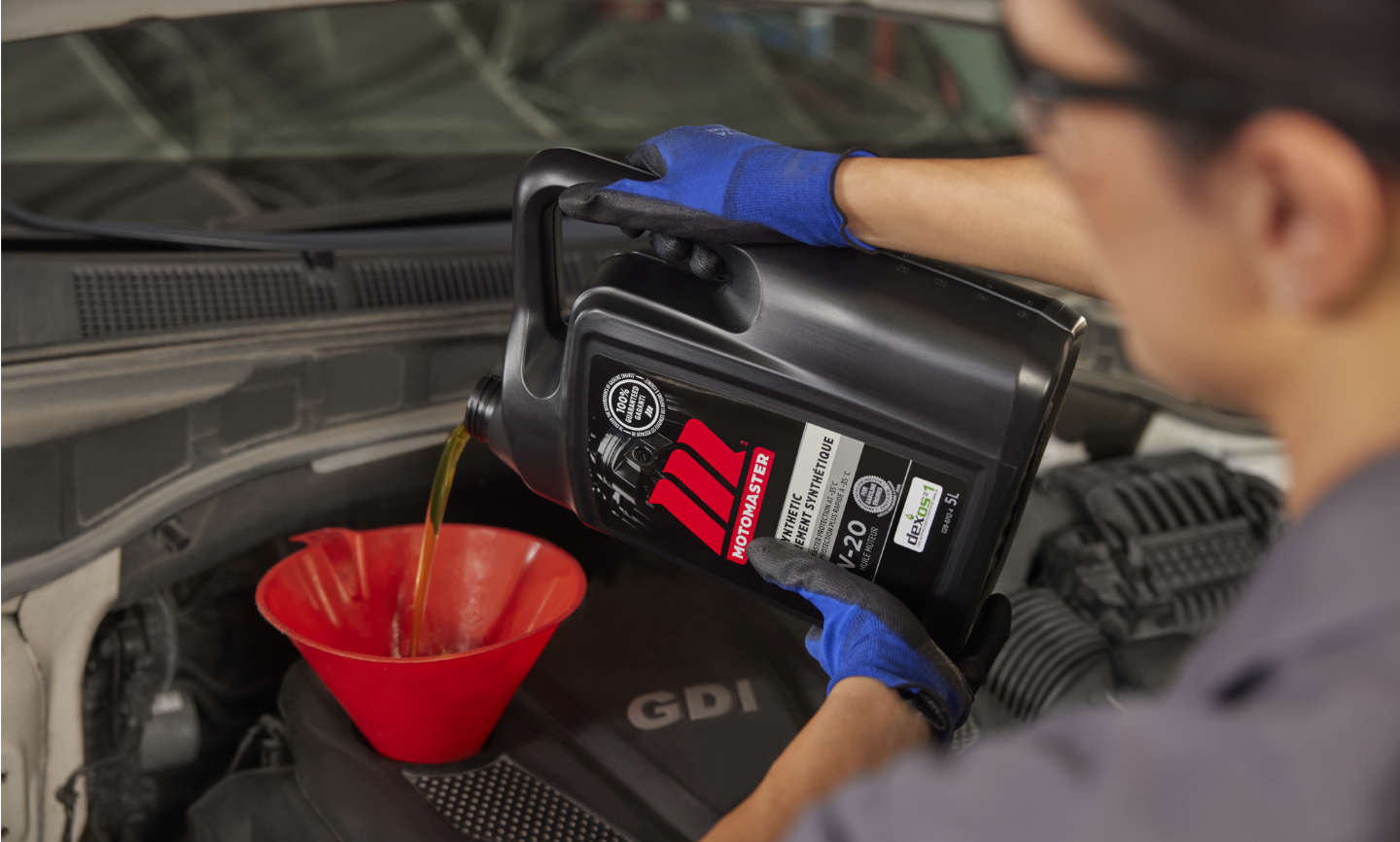 A person pours MotoMaster oil into an engine with a funnel.