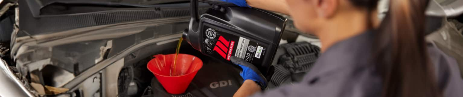 A person pours MotoMaster oil into an engine with a funnel.