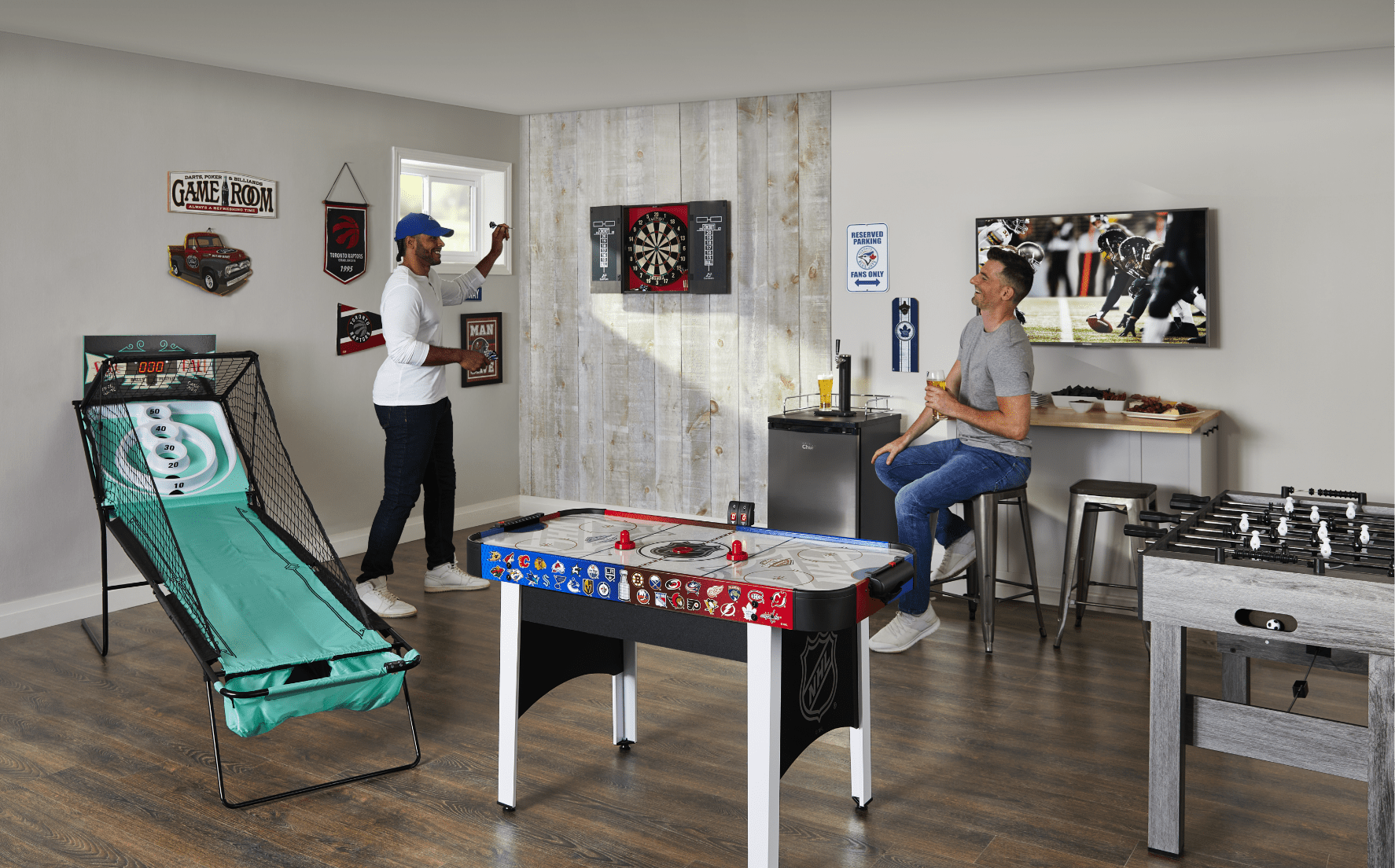 Two men watch football and play darts in a games room.