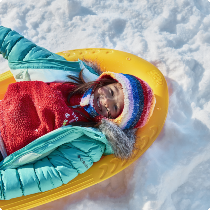 A smiling child rides a plastic toboggan.