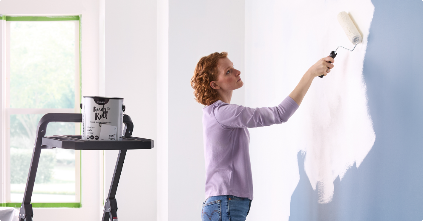 A person painting a wall white with a roller brush.