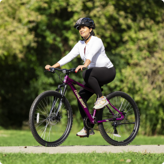 Une personne conduisant un vélo violet sur un sentier pavé dans un parc.